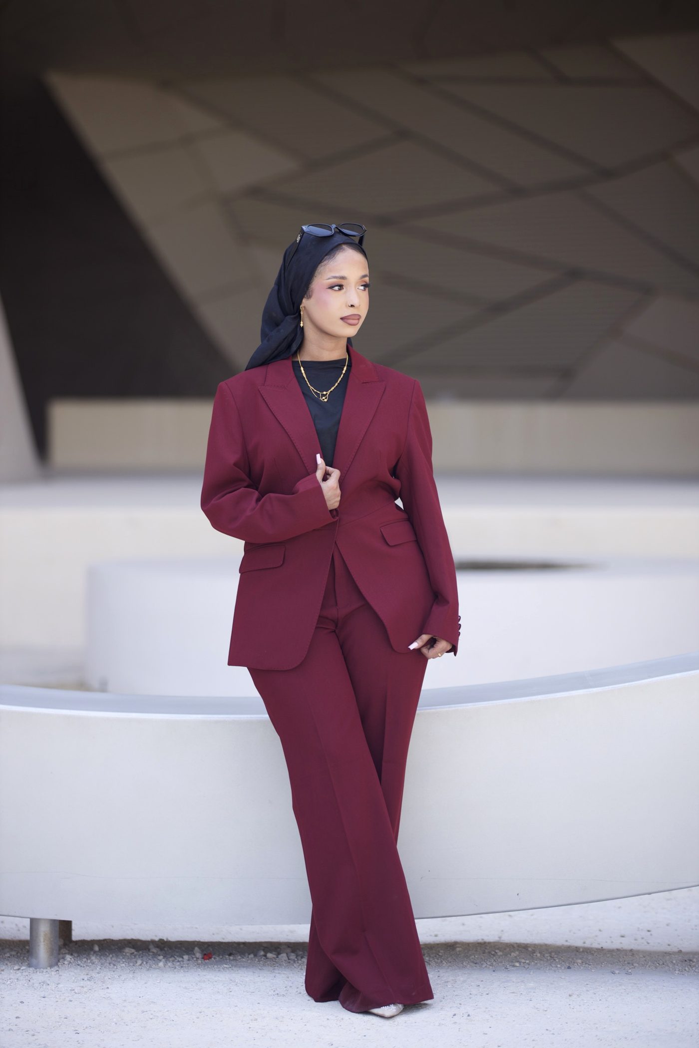 Woman in a wine three-piece suit standing before curved stone walls in Doha